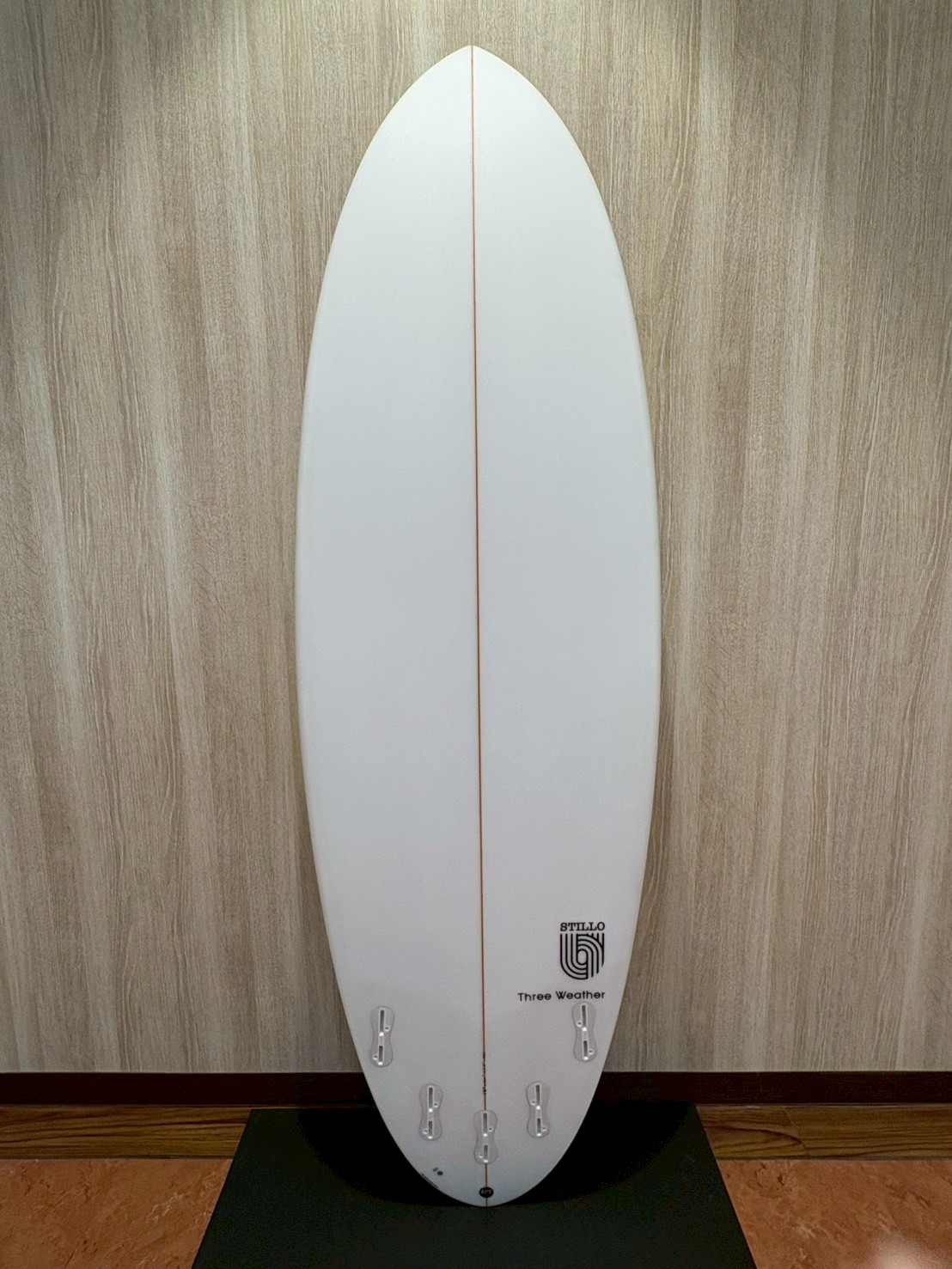 LINE_ALBUM_2026 TW_260422_11 - SHOP NEWS | ムラサキスポーツオンラインストア 通販 White surfboard standing upright indoors against a wood-paneled wall, with a thin center stringer and multiple fin boxes near the tail.