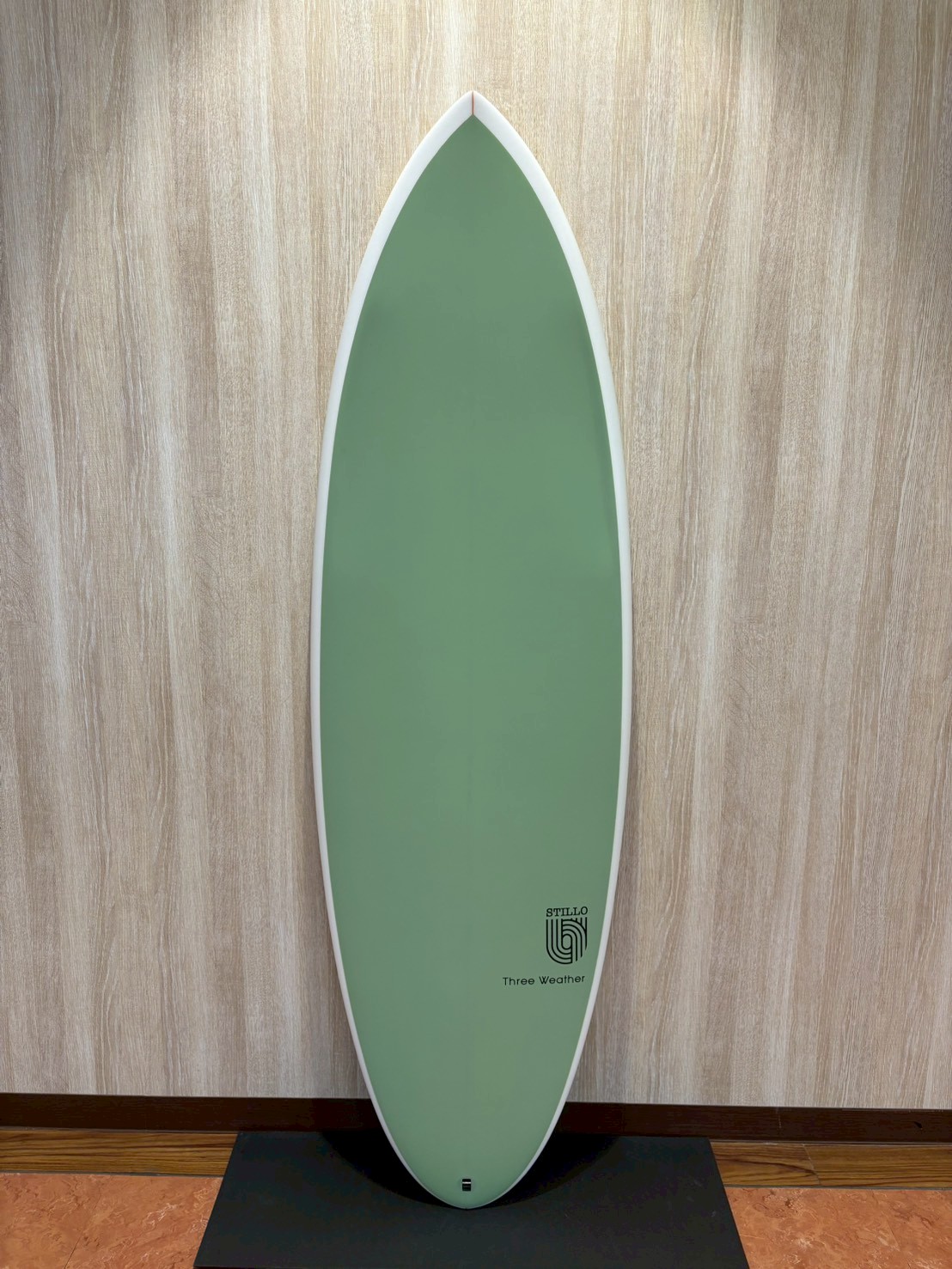 LINE_ALBUM_2026 TW_260422_7 - SHOP NEWS | ムラサキスポーツオンラインストア 通販 Green surfboard standing upright on a display pedestal indoors, with white edge and small logo near the bottom reading 'Three Weather'