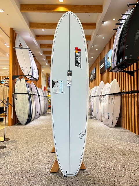 Light blue surfboard standing upright on a wooden stand in a surf shop, with other boards along the walls.