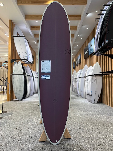 Purple surfboard on a display stand in a showroom, with racks of white boards along both walls.