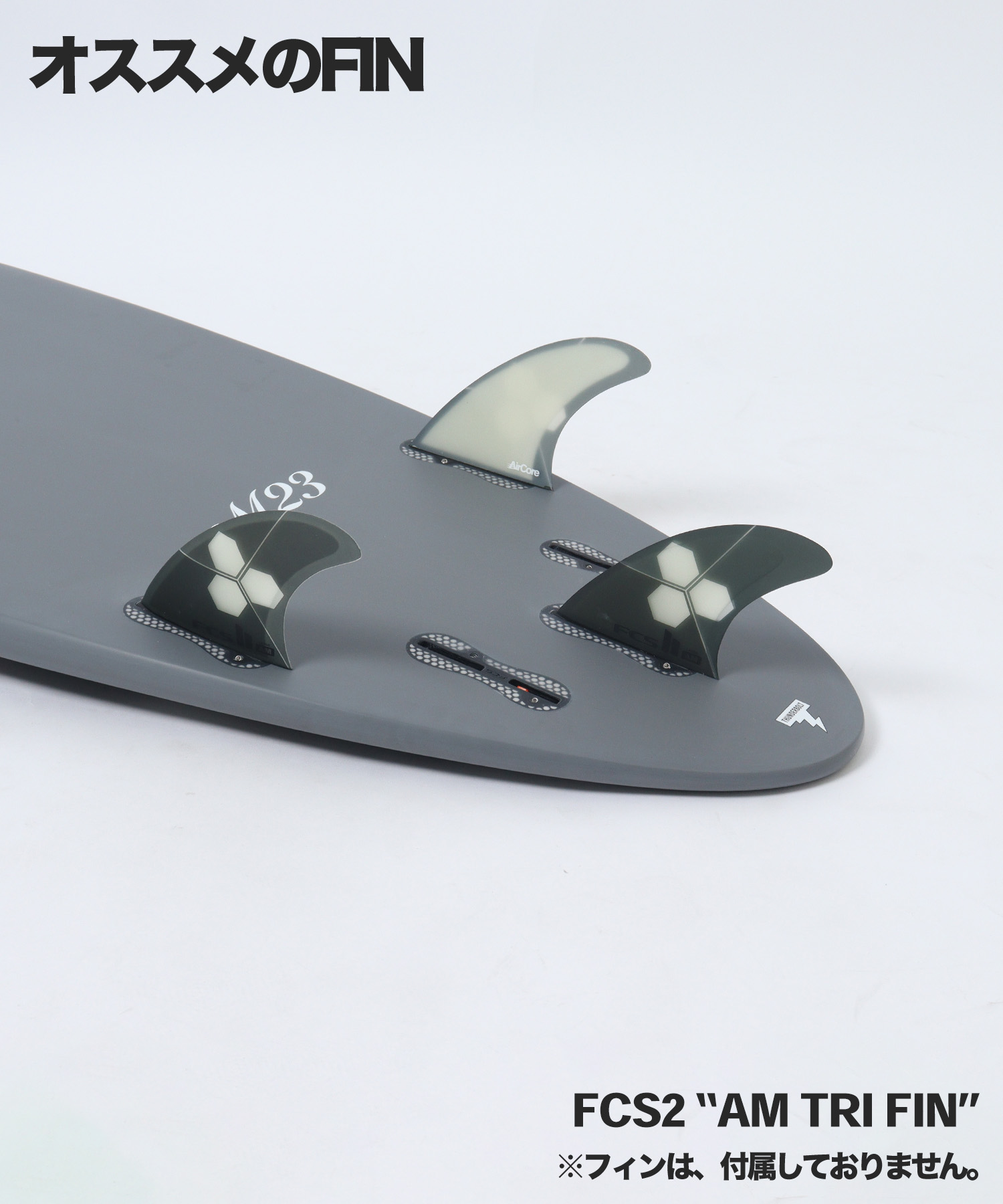 Close-up of a gray surfboard showing a three-fin setup: a translucent center fin and two darker side fins with hexagon logos (AM Tri Fin).