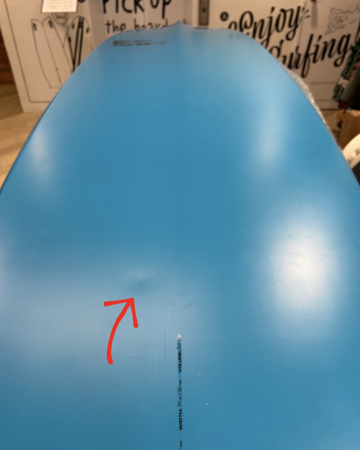 Blue inflatable board with a red arrow indicating a small surface scratch near the center. A vertical measurement line is also visible for scale.