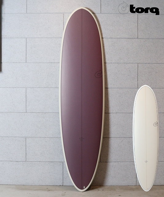s-n25111101110019 - SHOP NEWS | ムラサキスポーツオンラインストア 通販 Two surfboards leaning against a gray block wall: a large burgundy board on the left and a smaller white board on the right (Torq logo in the top-right).