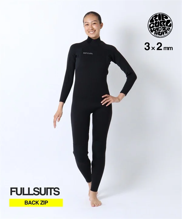 Woman modeling a black Rip Curl fullsuit with back-zip, 3×2 mm, standing with hands on hips.
